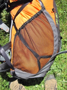 Vue latérale de la moitié basse du sac, vaste poche filet élastiquée en haut et sangle de compression qui serpente